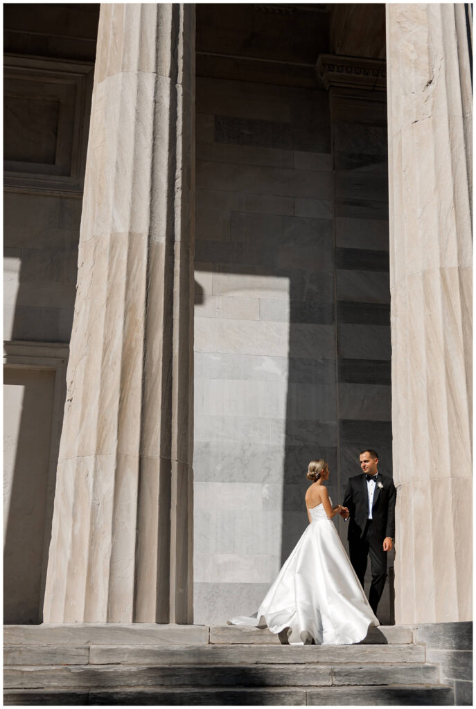 Elegant couple standing in the sunshine between two columns of a modern building. 