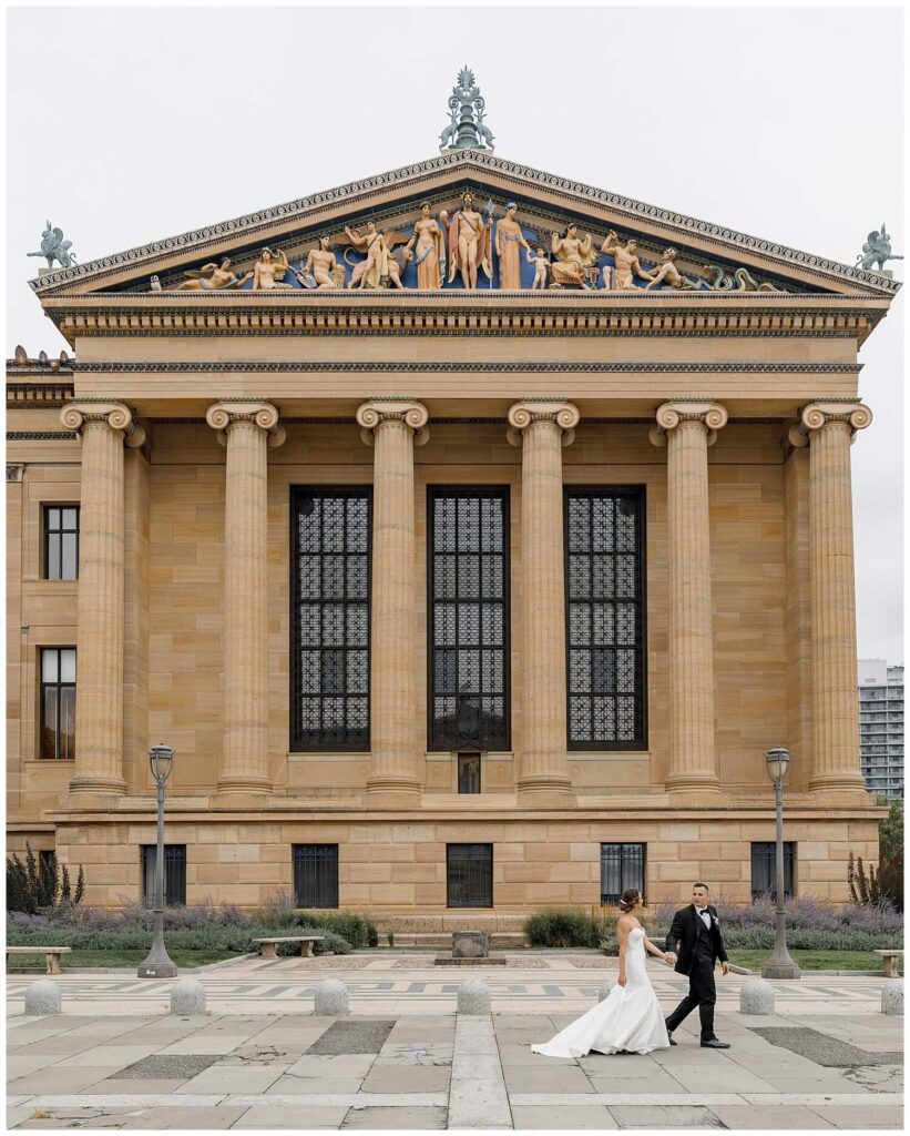 Bride and groom walking passed the front of the Art Museum of Philadelphia. 