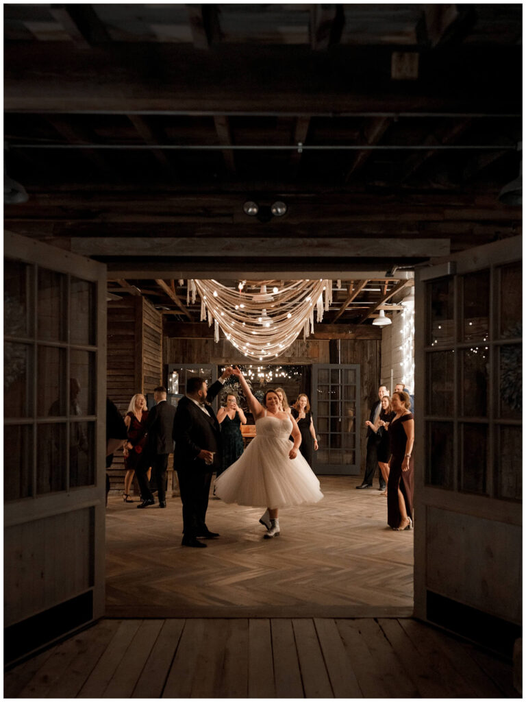 A couple, illuminated by one small light on a dark evening, sharing an intimate and romantic first dance on their wedding day in a rustic farmhouse setting.