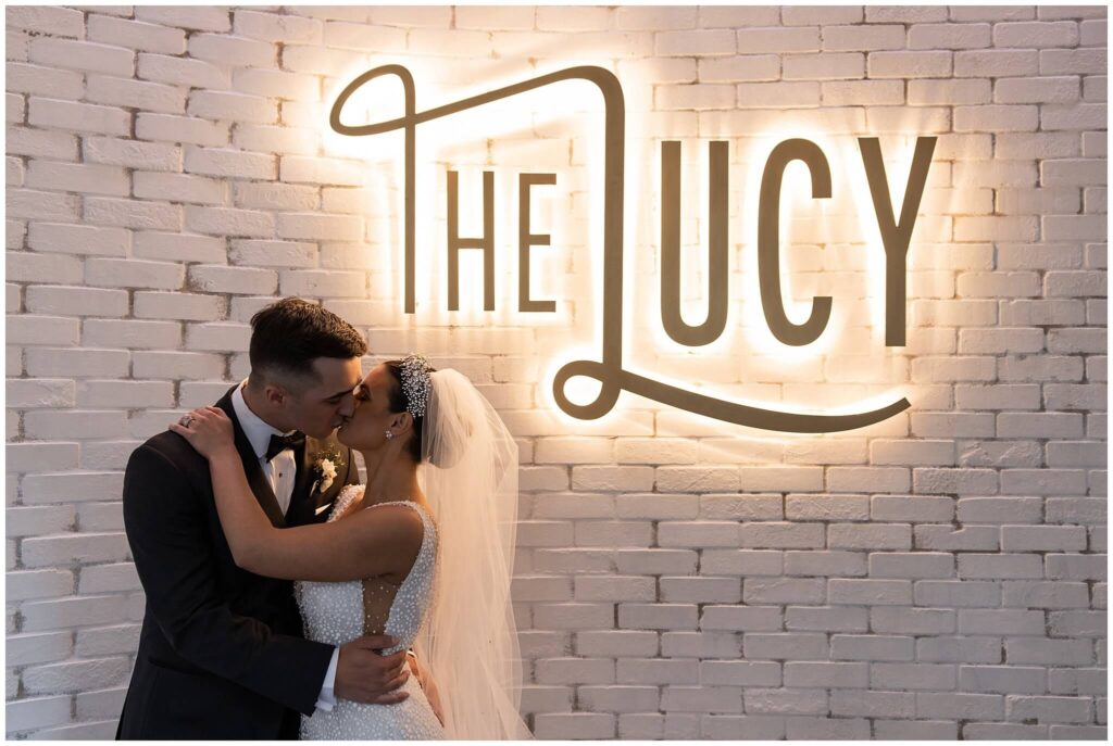 Young couple on their wedding day kissing in front of The Lucy sign at Cescaphe wedding venue in Philadelphia