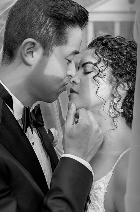 Groom softly touches his brides face as he leans in closer to share a kiss on their wedding day
